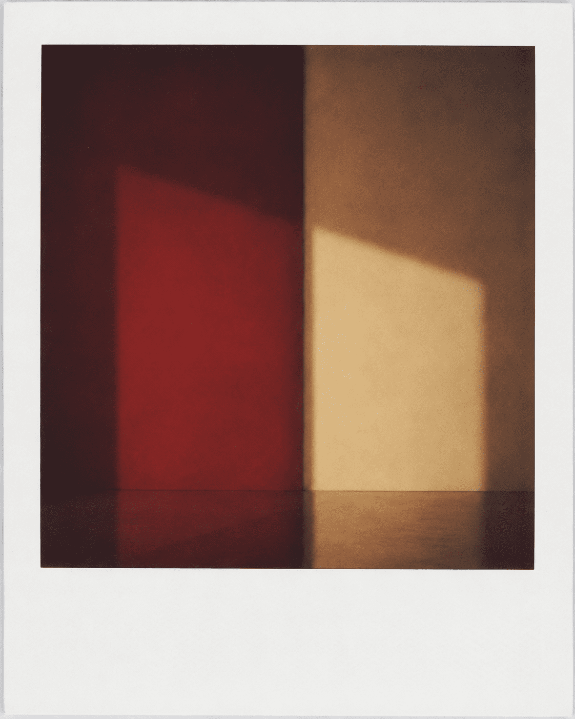 A single instant photograph of a red wall and a beam of morning light falling across a pale surface