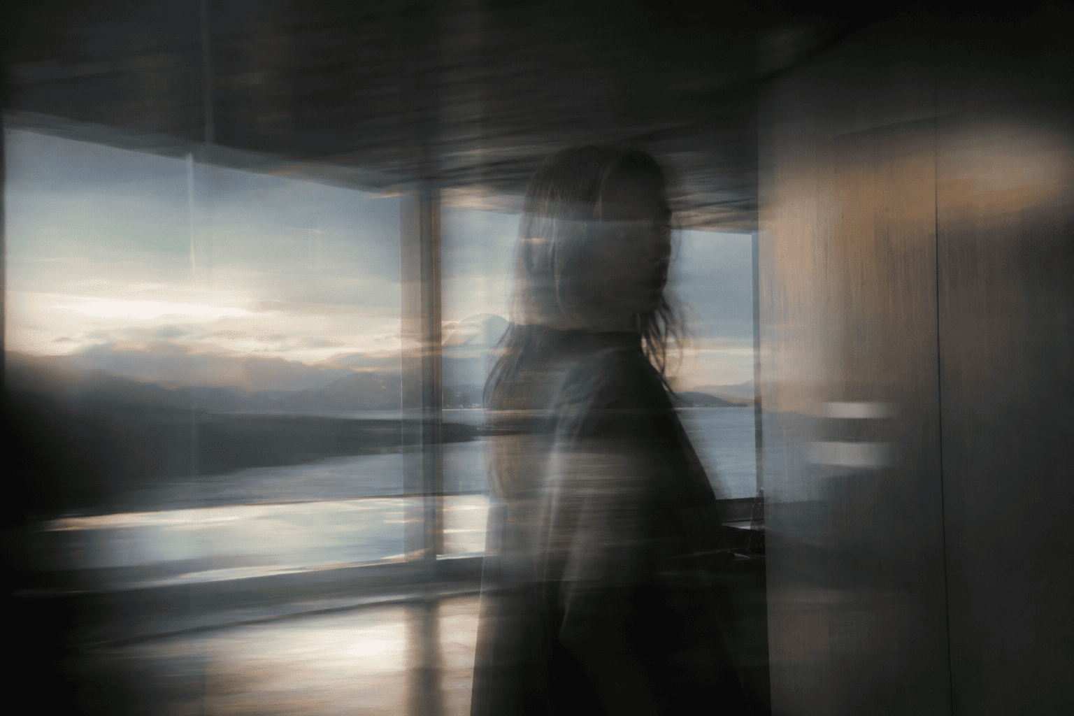 A blurred figure caught mid-motion inside a dim glass room, dissolving into horizontal streaks